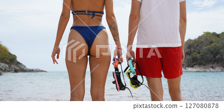 A woman in a bikini and man in red shorts holds snorkels before diving 127080878