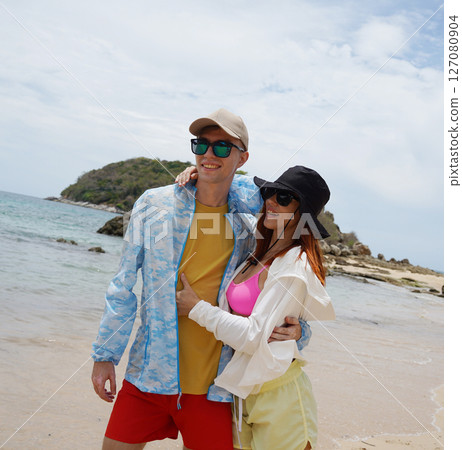 A young couple are leisurely walking along the beach, holding hands and enjoying the warm sun 127080904