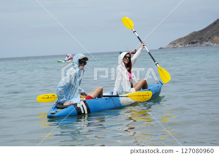 The young couple are happily navigating together in a light blue kayak with yellow paddles 127080960