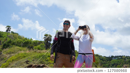 A man and a woman are intently looking through binoculars at something interesting in the distance 127080988