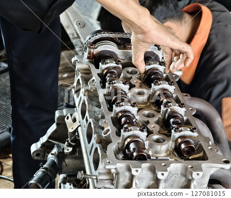 Two men are diligently working on a car engine inside a garage 127081015