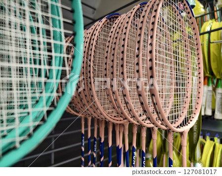 A nicely organized row of badminton rackets hanging on a rack in a store 127081017