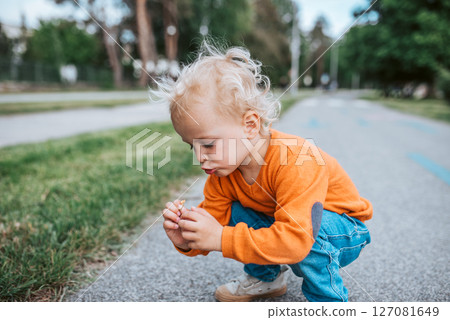 Curious toddler boy examines small flower outdoors. Curious toddler boy examines small flower outdoors. 127081649