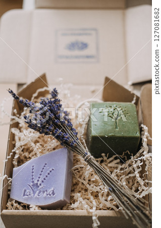 Lavender and olive oil soaps with dried flowers in a kraft gift box filled with shredded filler. Botanical skincare, handmade soap, natural ingredients, eco-conscious packaging 127081682