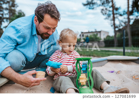 Father and little toddler son playing in the sandbox on playground. Father and little toddler son playing in the sandbox on playground. 127081699