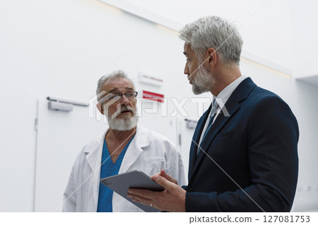 Doctor talking with hospital manager, showing him document in tablet. Doctor talking with hospital manager, showing him document in tablet. 127081753