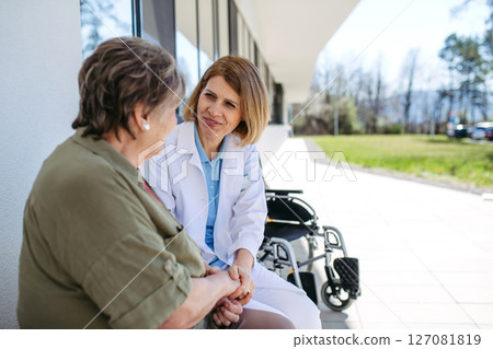 Doctor and elderly patient sitting in front of hospital building and talking. 127081819