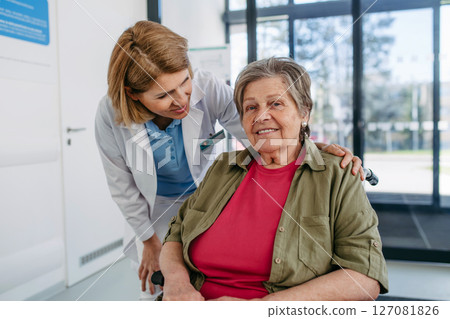 Geriatric doctor talking with patient in a wheelchair in hospital hallway. 127081826