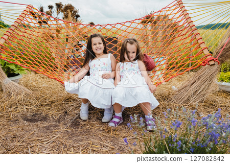 Two girls in white dresses are swinging on a red mesh hammock 127082842