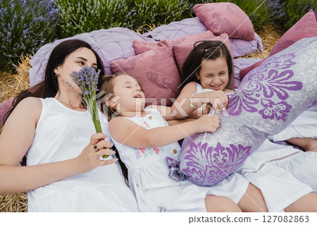 The mother and her daughters lie on a bed covered with a purple blanket, in the center of the lavender field 127082863
