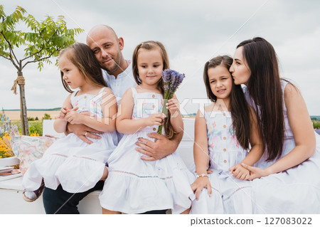 The parents and daughters relax on an old-fashioned bench in a blooming field 127083022