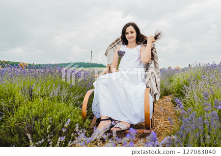 A young woman in a long white dress sits on a rocking chair in the middle of a lavender field 127083040
