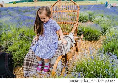 A girl with long, loose hair and a purple dress is sitting in a rocking chair in a lavender field 127083427