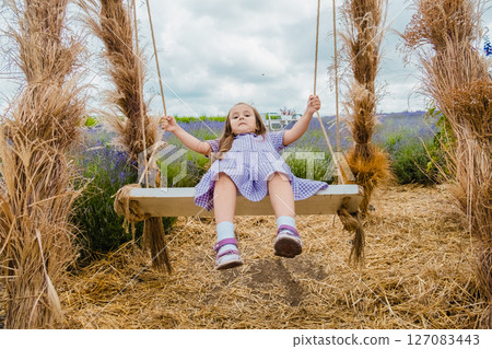 A young beauty laughs happily as she swings on a large swing in a lavender field 127083443