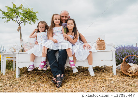 On an old-fashioned bench in the lavender field, a happy father sits with his three daughters 127083447