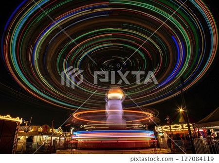 Long exposure circular light patterns created by spinning carnival ride against dark night sky at summer fairground 127084119