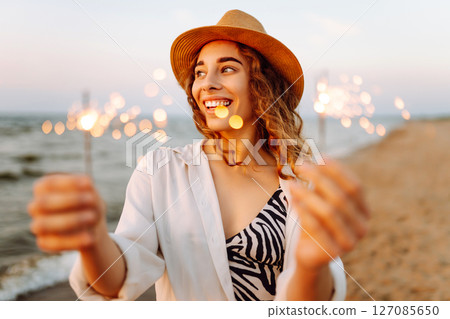 The sparklers in hands of young woman on the beach. Woman enjoying party on beach with sparklers. 127085650