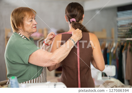 Mature woman seamstress takes measurements from a girl 127086394
