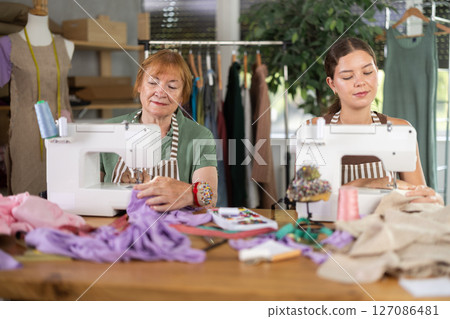 Elderly and young women seamstresses sewing on machine 127086481