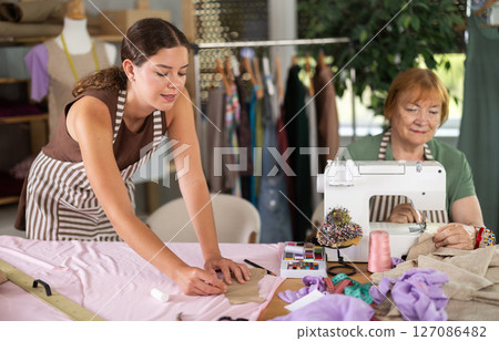woman dressmaker makes markings on the fabric next to the seamstress 127086482
