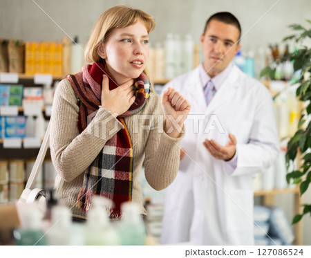 Young woman having sore throat while pharmacist offering in drugstore 127086524