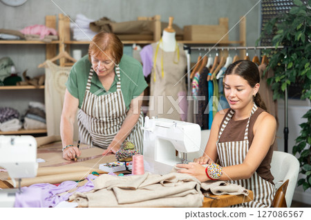Mature dressmaker drawing patterns next to young assistant 127086567