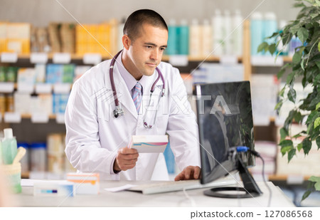 Male pharmacist standing at drugstore with medical product in hands 127086568