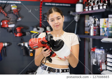 Woman chooses and buys paint spray gun in hardware store Woman chooses and buys paint spray gun in hardware store 127086665