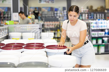 Woman chooses and buys can of paint at hardware shop 127086689
