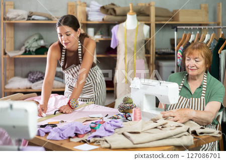 Elderly woman sewing, young woman drawing on fabric Elderly woman sewing, young woman drawing on fabric 127086701