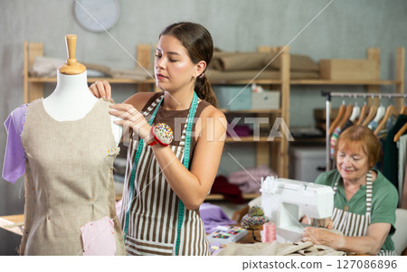 Woman working with mannequin against the background of an elderly dressmaker Woman working with mannequin against the background of an elderly dressmaker 127086896