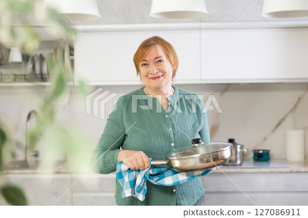 Portrait of a mature smiling woman with a frying pan in her hands Portrait of a mature smiling woman with a frying pan in her hands 127086911