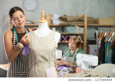 Young woman working with mannequin, elderly woman sewing Young woman working with mannequin, elderly woman sewing 127086944