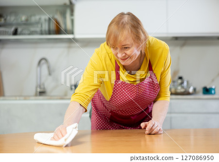 Hardworking mature woman wipes the table with a damp cloth Hardworking mature woman wipes the table with a damp cloth 127086950