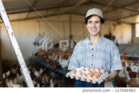 Young Latin female farmer worker holding cardboard box full of fresh chicken eggs on poultry farm Young Latin female farmer worker holding cardboard box full of fresh chicken eggs on poultry farm 127086962