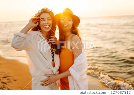 Portrait of two young female friends walking on the sea shore at sunset. Lifestyle concept. 127087512