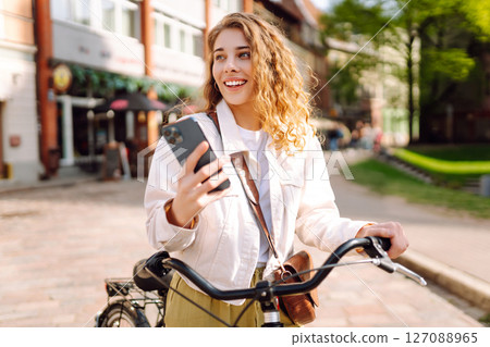 Young woman using mobile phone while riding bicycle at the city street outdoor. Selfie time. 127088965