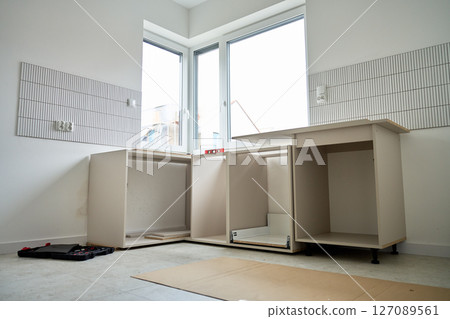 Partially installed kitchen base cabinets without countertops in bright interior. Process of furniture fitting and renovation in new apartment 127089561