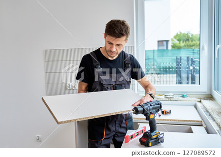 Man in uniform measures cabinet panel during kitchen furniture installation. Renovation process in new apartment 127089572