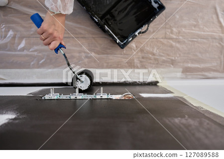 Detailed view of person using roller to paint wall black near electrical sockets during home renovation Detailed view of person using roller to paint wall black near electrical sockets during home renovation 127089588