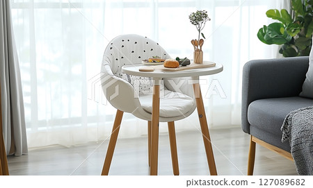 A white chair is sitting at a table with a vase of flowers and a plate of food 127089682
