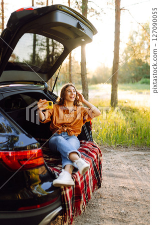 Happy Woman is resting in trunk of car and taking selfie. Selfie time. Lifestyle, travel 127090055
