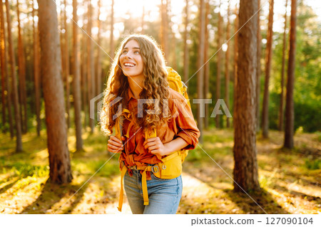 Tourist woman hiking alone in thick autumn forest. Stylish female looks for pathway among trees. Tourist woman hiking alone in thick autumn forest. Stylish female looks for pathway among trees. 127090104