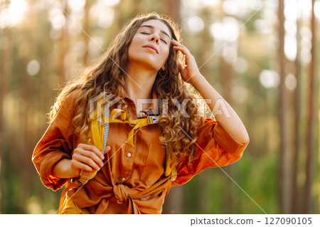 Tourist woman hiking alone in thick autumn forest. Stylish female looks for pathway among trees. Tourist woman hiking alone in thick autumn forest. Stylish female looks for pathway among trees. 127090105