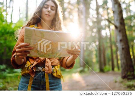 A traveler woman stands in a lush forest, examining a map with a focused expression 127090126