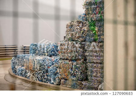 Compressed plastic bottles stacked outside recycling facility in sunlight 127090683