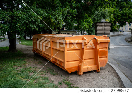 Large orange industrial dumpster placed under trees in urban park area outdoors Large orange industrial dumpster placed under trees in urban park area outdoors 127090687