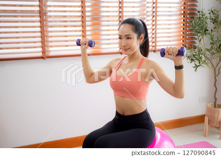 Young asian woman in sportswear workout with dumbbells for strength in living room. Young asian woman in sportswear workout with dumbbells for strength in living room. 127090845