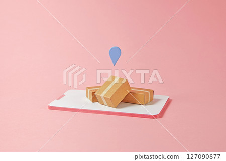 On a pretty pink background, mini cardboard boxes and a blue pin lie on top of a paper smartphone. Symbolizes mobile apps as the central hub for consumer purchases and discounts. 127090877