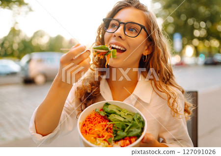 Young tourist standing in the middle of the street, eating takeaway lunch while taking in the sights 127091026